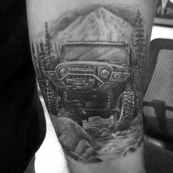 Realistic black and grey tattoo of an off-road Jeep navigating rocky terrain, surrounded by tall pine trees and a towering mountain backdrop.