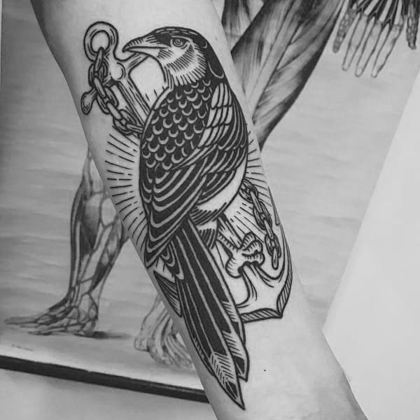Blackwork magpie tattoo on forearm, featuring bold linework with the bird holding a chain and anchor, symbolizing strength and resilience.