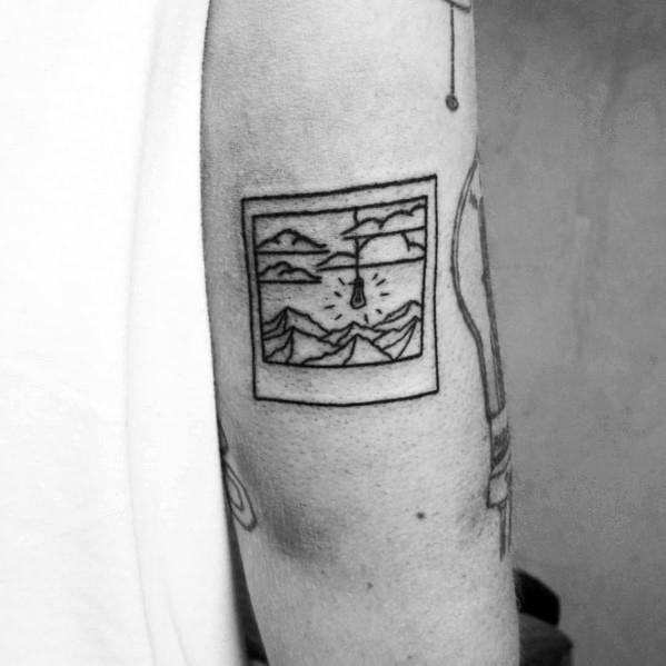 Minimalist framed mountain tattoo on the upper arm, featuring a fine line landscape with peaks, a river, and a sun or moon for a scenic design.