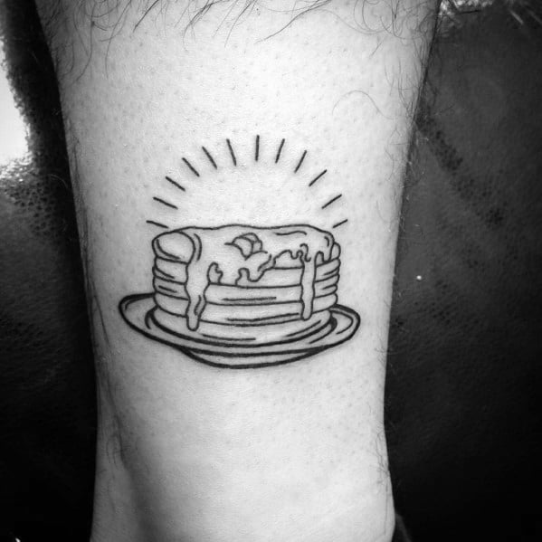 Minimalist black ink pancake tattoo with syrup and butter on a plate, featuring bold outlines and radiating lines for a classic look.