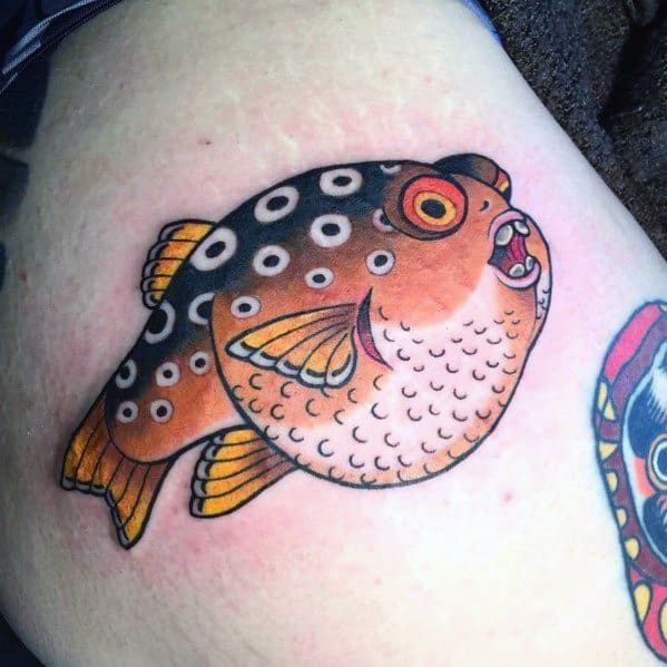 Bold pufferfish tattoo with black and orange hues, intricate dot patterns, and a classic traditional style, creating a striking visual effect.