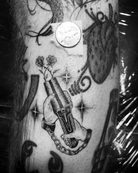 Black and grey tattoo of hands holding a double-barrel shotgun with flowers emerging from the barrels, symbolizing a mix of power and peace.