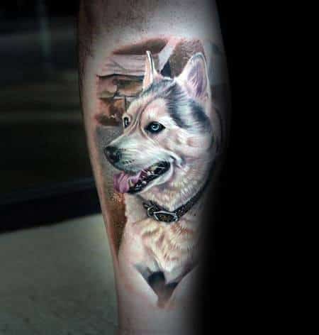 Hyper-realistic Siberian Husky tattoo on a man's leg, featuring intricate fur details, lifelike blue eyes, and a scenic background for depth.