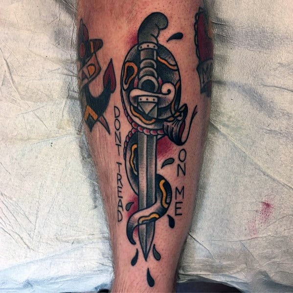 Traditional snake and dagger tattoo on leg, featuring bold black, red, and yellow ink with "Don't Tread on Me" lettering and blood drops.