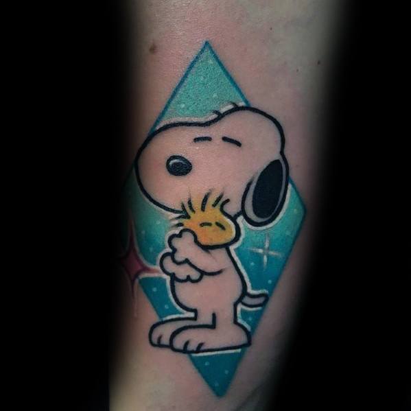 Colorful tattoo of Snoopy hugging Woodstock with a blue diamond-shaped background and sparkles, placed on a person's forearm.