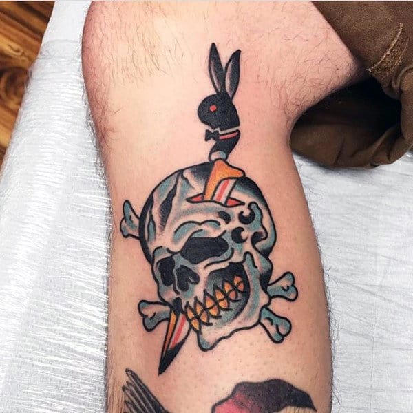 Male With Traditional Tattoo Of Dagger And Skull On Lower Leg