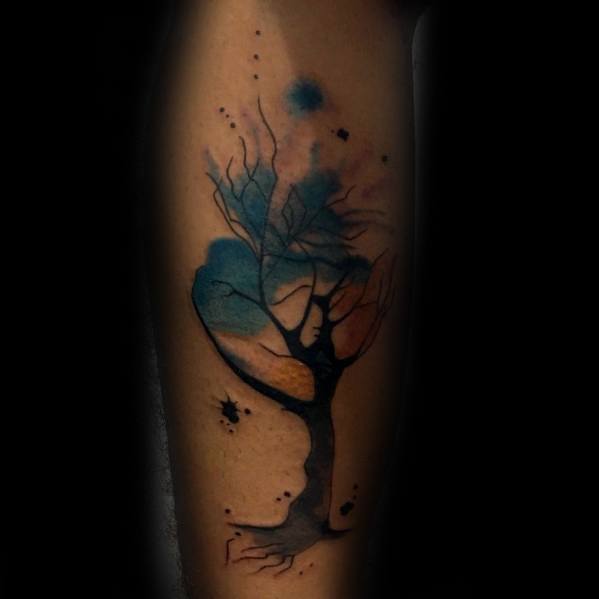 Watercolor tree tattoo on the leg, featuring abstract blue and orange splashes blending with bare branches for a dreamy, artistic design.
