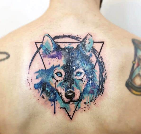 Watercolor wolf tattoo on upper back with cosmic blue and purple tones, geometric triangle framing, and subtle starry details.
