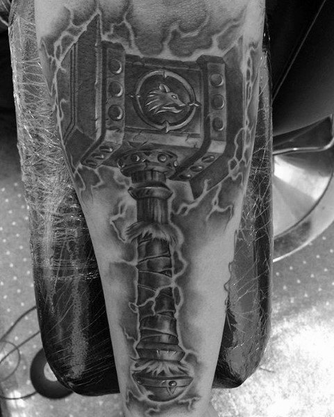 Realistic black and grey tattoo of Doomhammer from World of Warcraft, featuring intricate details, lightning effects, and a powerful design, inked on the forearm.