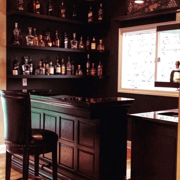 Home bar with shelves of bottles, a leather stool, and a window with patterned glass