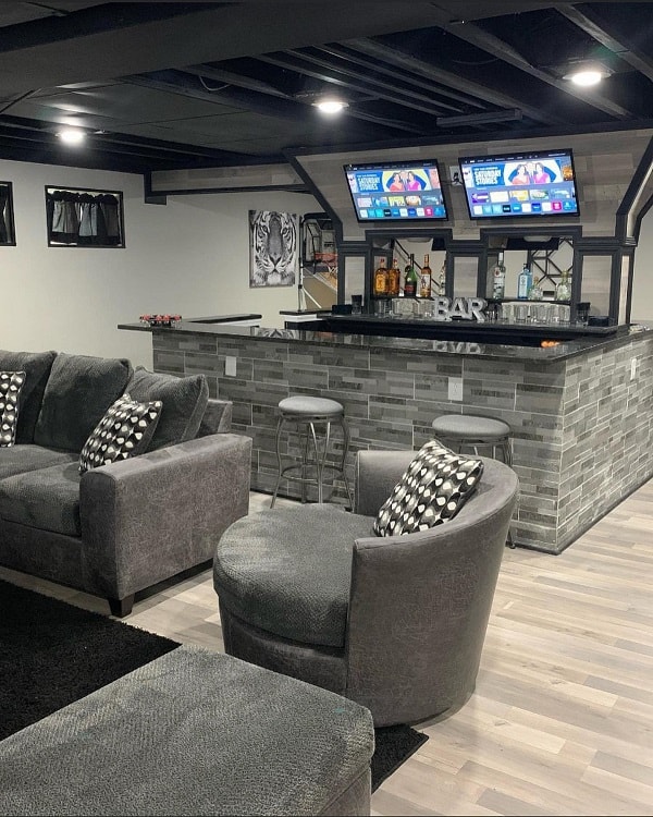 gray tile basement bar black countertop dual tvs gray couch and sofa 