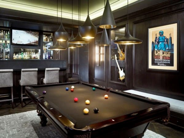 Stylish game room with a pool table, bar, hanging lights, and framed art on dark wood walls