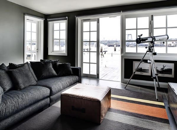 Modern living room with a black sofa, a telescope by large windows, and a striped rug on the floor