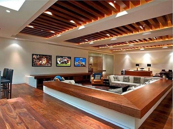 Modern man cave room with wooden ceiling and floor, sectional sofa, and sports images on the wall