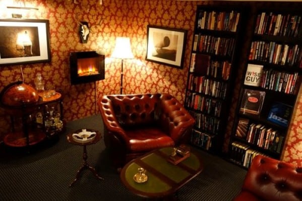 Cozy study with a red leather armchair, bookshelves, globe bar, and a warm fireplace