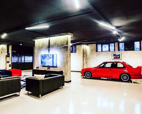 A sleek garage with a polished floor, black ceiling, and a lounge area complemented by a striking red car.