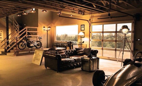 A warm, rustic dream garage featuring a leather couch, motorcycle, and large windows offering scenic views.