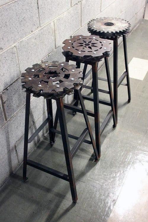 Three industrial metal stools with gear-shaped seats against a concrete wall