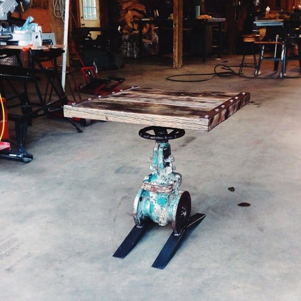 A rustic industrial table with a wooden top and metal base in a workshop setting