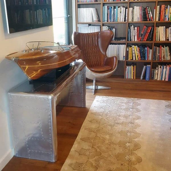 Modern study with a sleek desk, leather chair, model ship, bookshelves, and a patterned rug