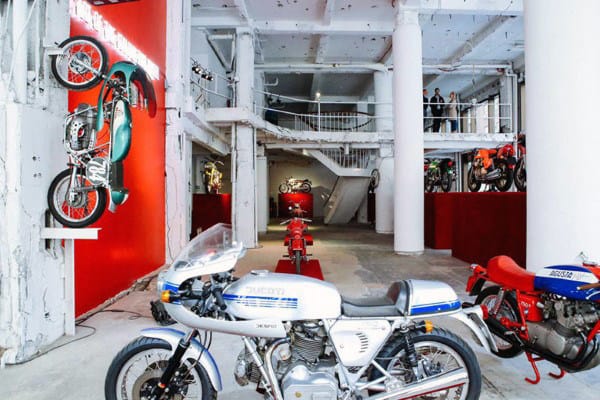 Motorcycle exhibition in a spacious garage, featuring bikes on display with red accents and a multi-level setup