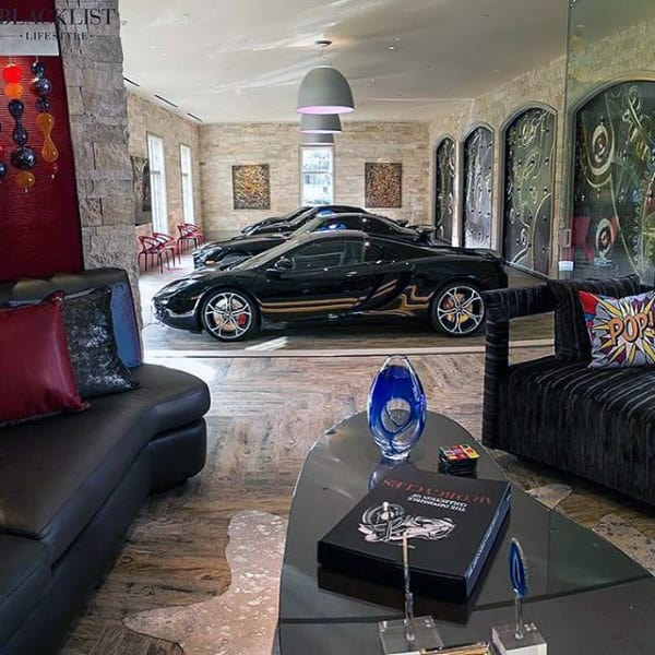 Luxury room with three black sports cars in an indoor garage, modern décor, and decorative pillows on a black couch
