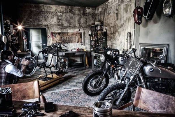 A vintage motorcycle garage with bikes, tools, and a mechanic hard at work