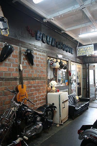 Vintage-themed garage room with a motorcycle, guitar, retro fridge, and "The Blue Groove" sign on a brick wall