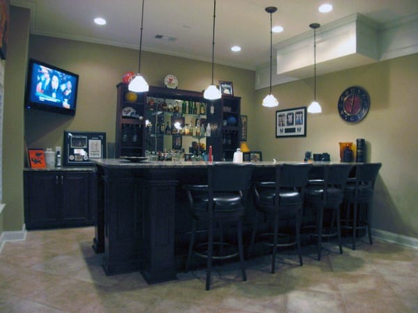 Bar area with high chairs, overhead lights, a TV, and shelves stocked with bottles and glasses