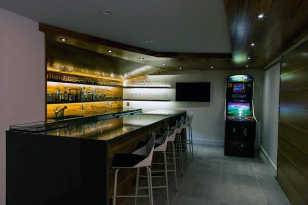 A modern bar with stools, a wall-mounted TV, and an arcade machine