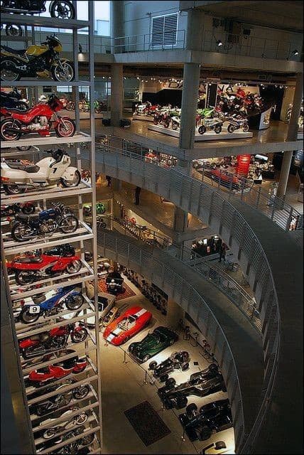 Interior of a multi-level museum resembling a garage, showcasing motorcycles and cars with curved walkways