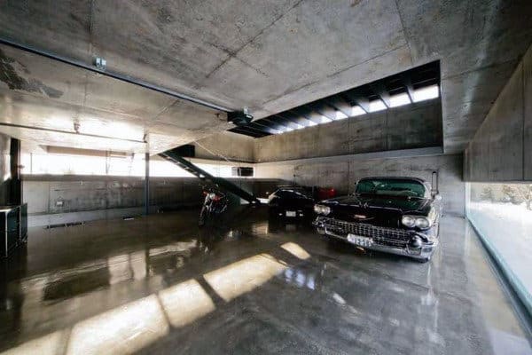 Minimalist garage with concrete walls, a vintage car, a modern ride, and motorcycle alongside a sleek staircase
