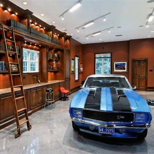 Vintage blue car parked in a library-like garage with a ladder, bookshelves, and framed art on the walls