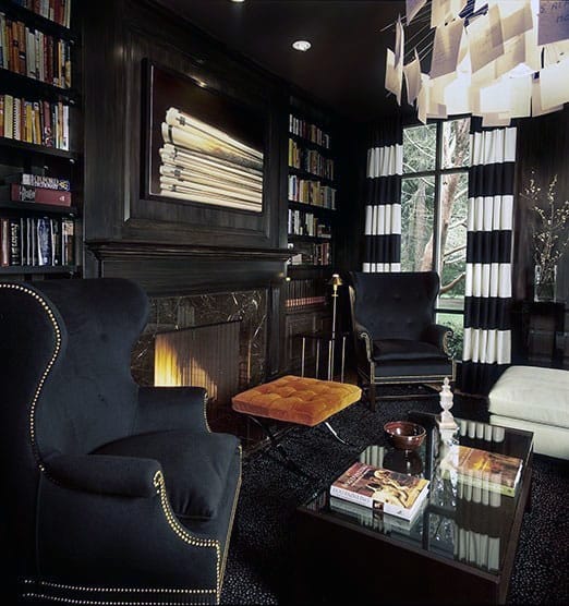 Sophisticated library with dark decor, armchairs, fireplace, bookshelves, and a glass coffee table