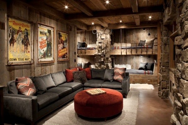 Rustic living room with a sectional sofa, vintage posters, stone walls, and built-in bunk beds