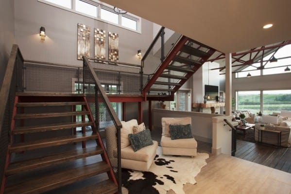 Modern loft-style living room with a metal staircase, cowhide rug, and large windows overlooking greenery