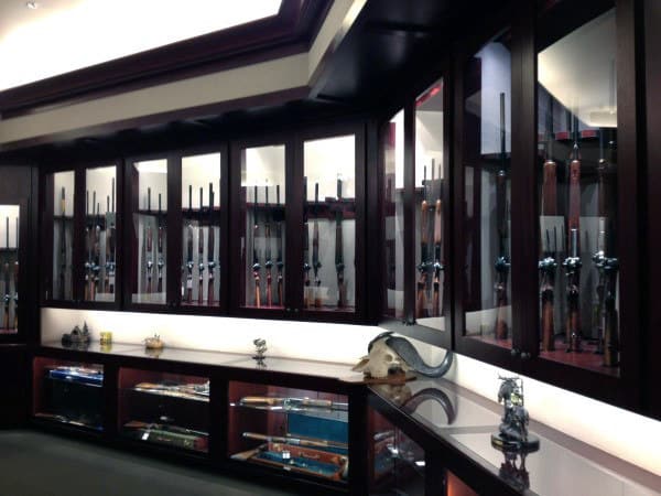 A sleek man cave featuring polished wood cabinets, glass display cases for rifles, and decorative accents like skull mounts and sculptures.