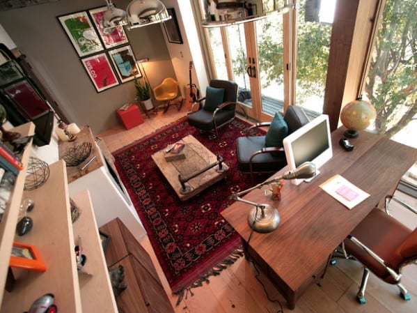 Aerial view of a cozy home office with a desk, lounge area, red patterned rug, and large windows overlooking trees
