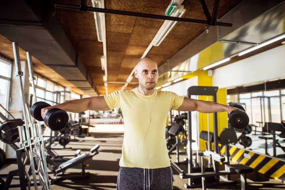strong muscular man doing trap raise shoulder exercise in gym