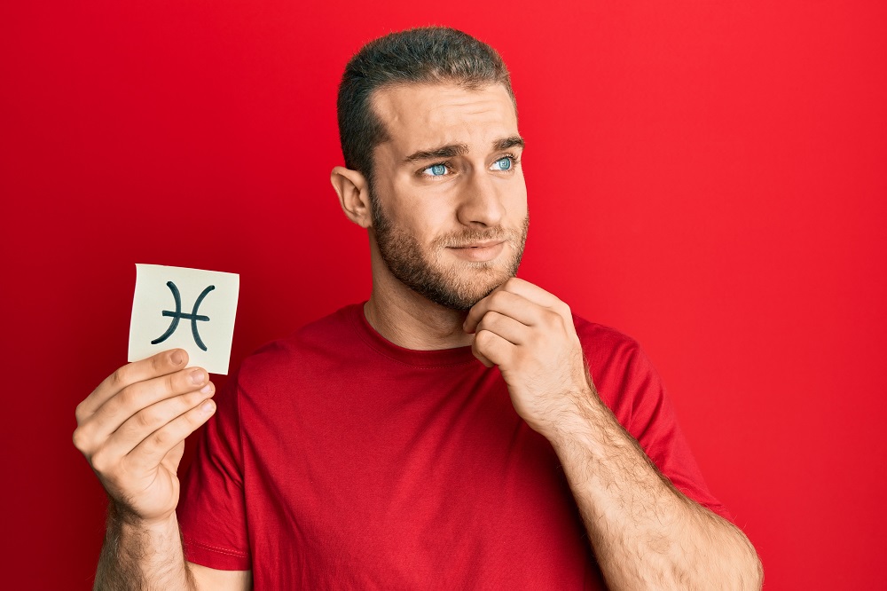man holding paper with pisces zodiac sign while thinking about question