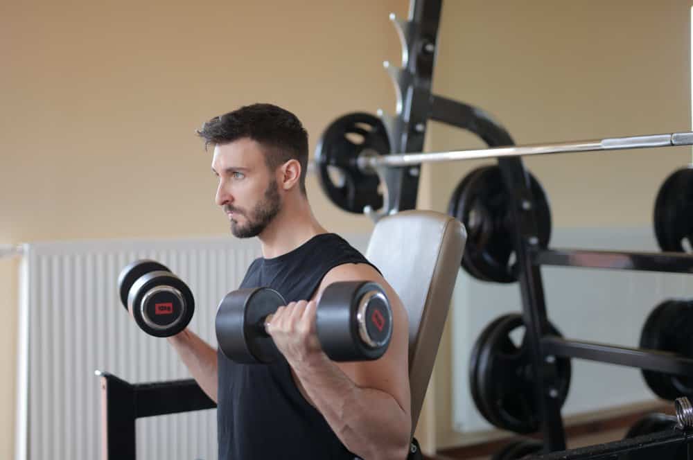 man holds a dumbbell in each hand, holding them upright towards his shoulders