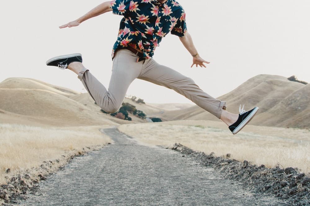 man jumping in mid-air, wearing khaki chino pants and a floral patterned button up shirt
