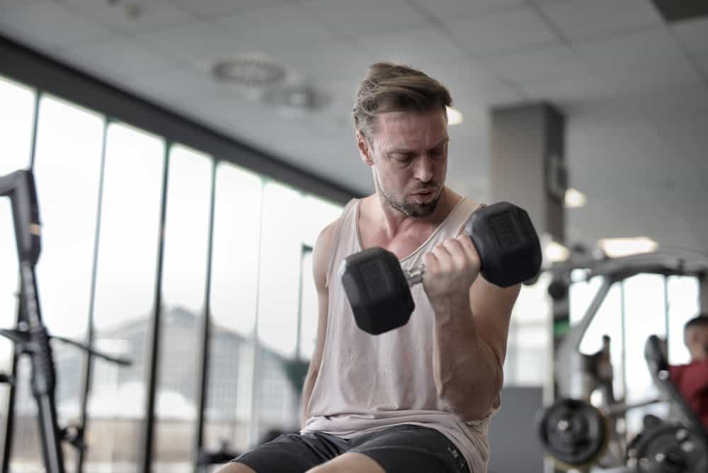 man sitting on a workout bench lifts a dumbbell
