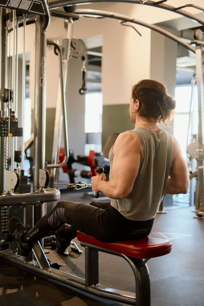 man in a gym performs a cable row, sitting on the bench and pulling inward on the cable machine