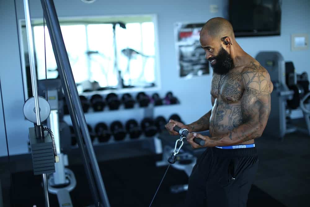 man in a gym performs a standing cable curl on a piece of gym equipment