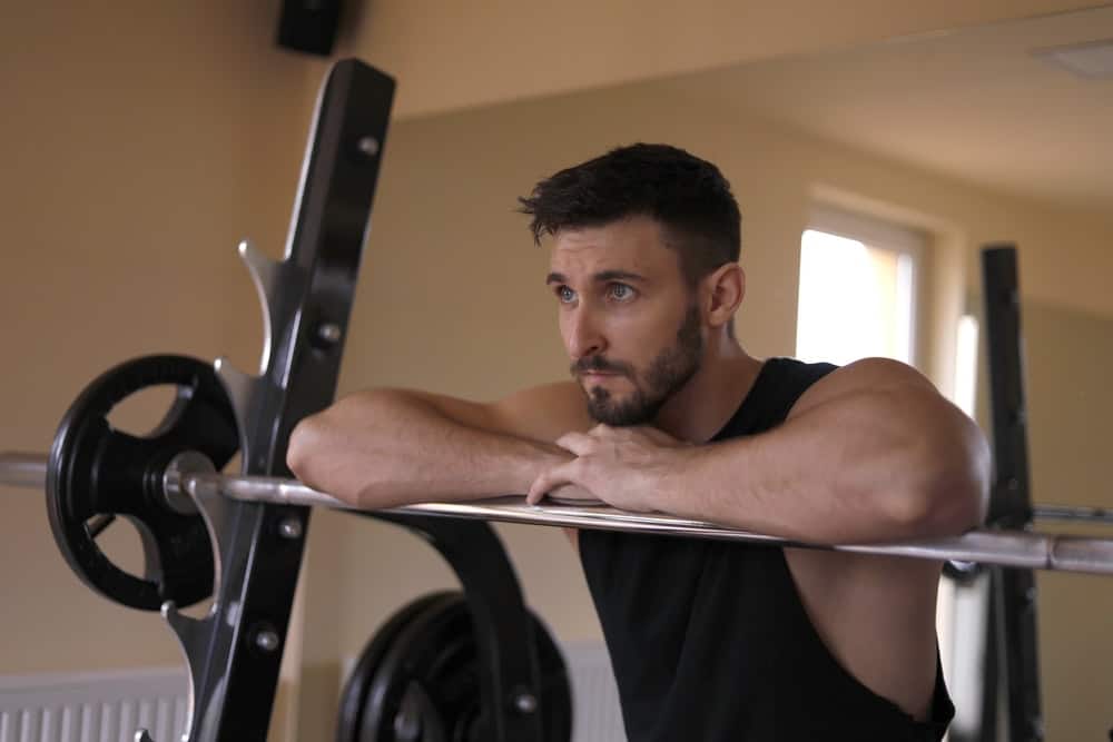 man rests his forearms on a barbell bar during training, looking forward