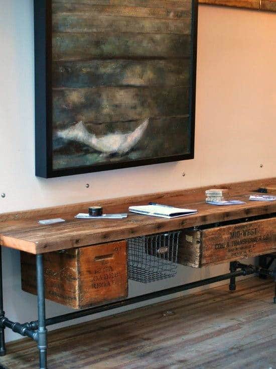 Rustic desk with wooden crates, metal pipe legs, and a framed abstract painting above