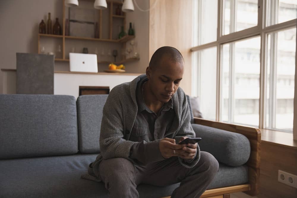 man sits on his couch at home, looking at his phone
