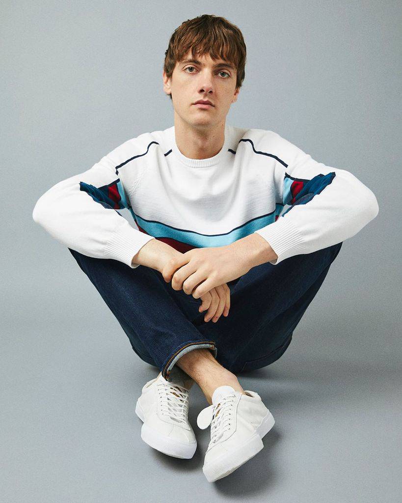 A man sitting cross-legged and wearing jeans that have been rolled at the cuff