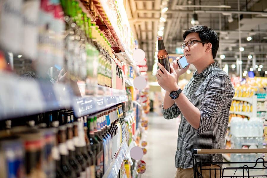 man using smartphone while shopping beer in supermarket